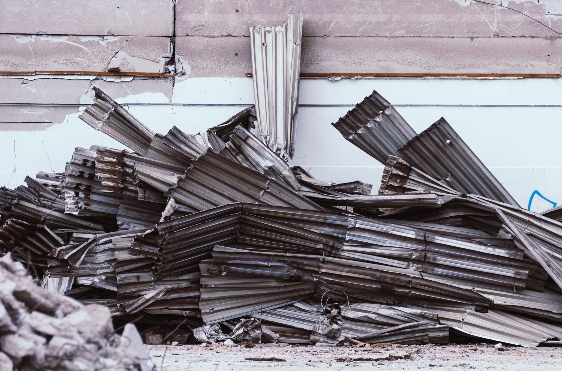 Pile of corrugated metal sheets against a worn industrial wall.